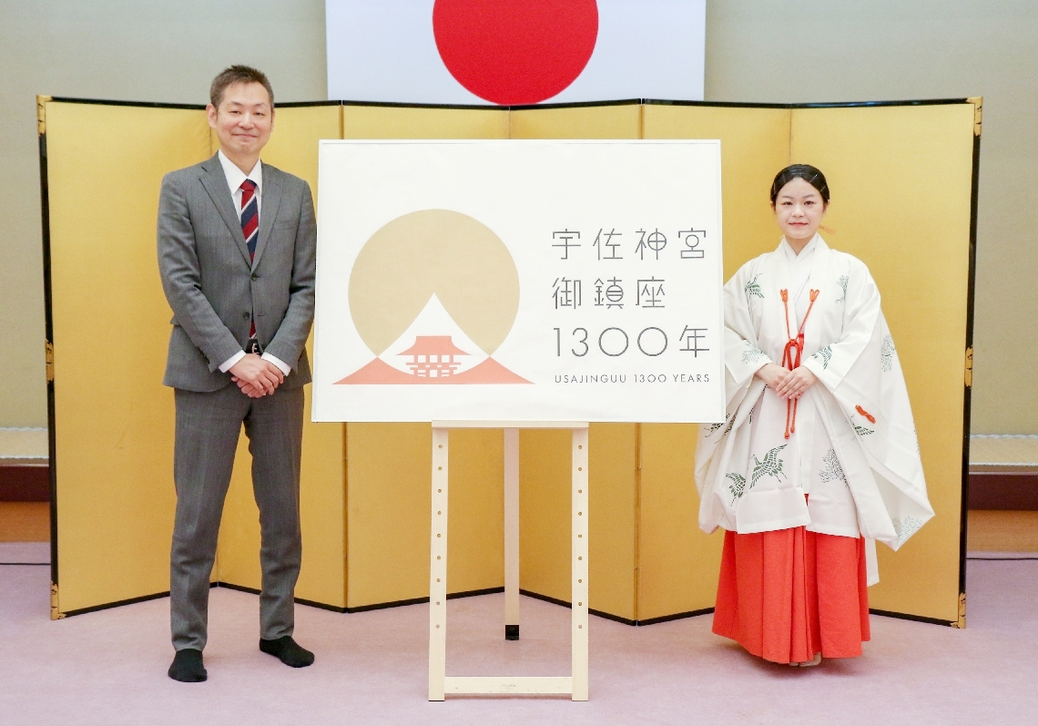 作品が御鎮座１３００年のロゴマークに採用された青山正樹さん（左）＝宇佐市南宇佐の宇佐神宮