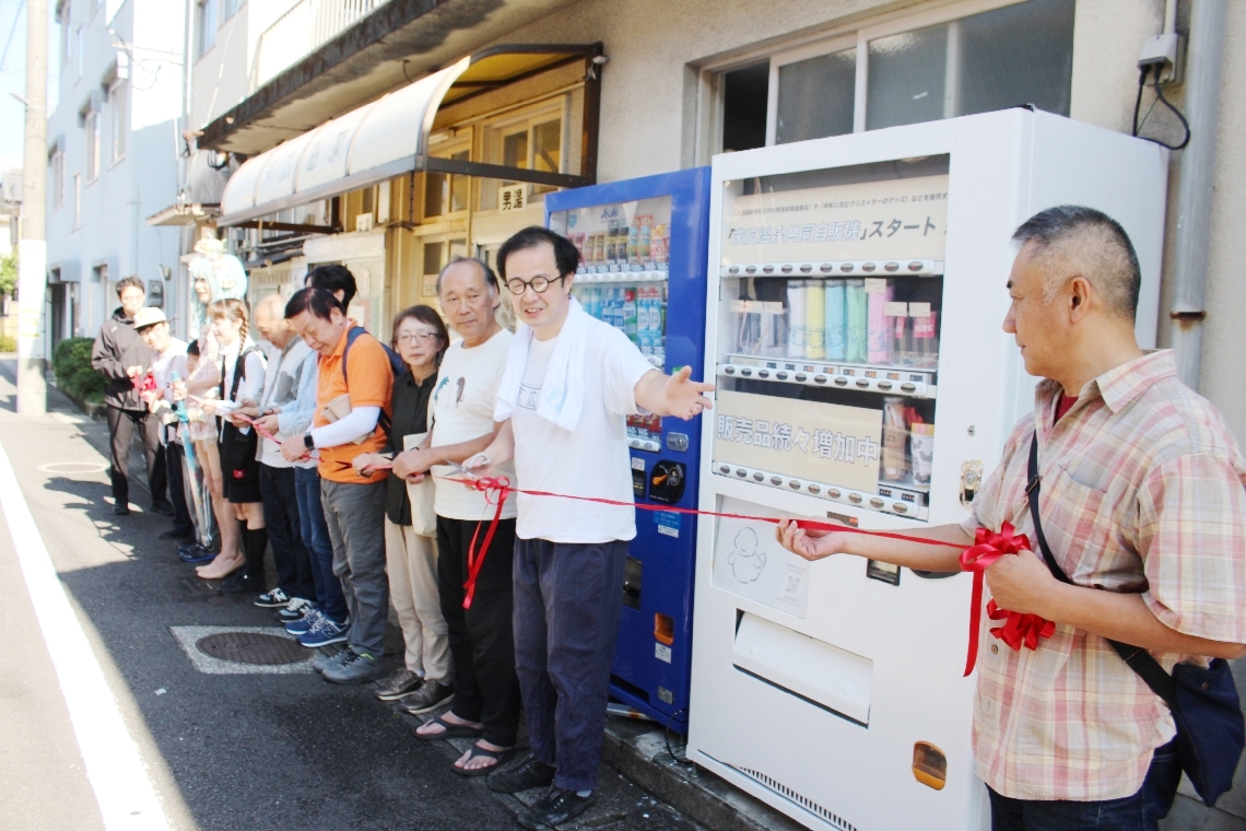 自動販売機機の稼働を祝う末広温泉の関係者や地域の人たち
