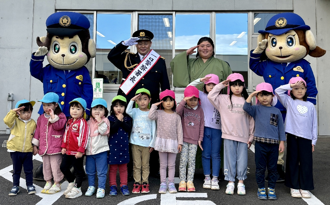 「一日署長」のたすきを着けて記念撮影をする雷親方＝２８日、大分東署