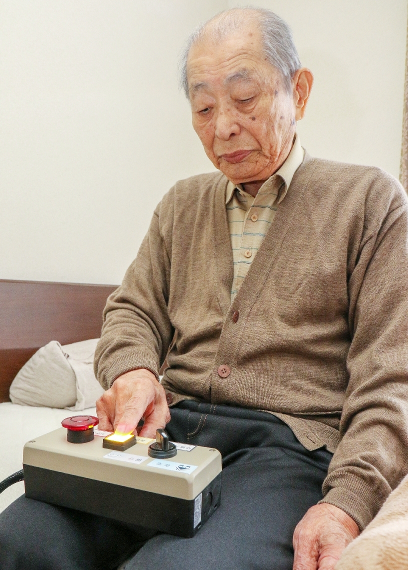 ベッド脇に装置を置き、「防犯対策にもなりそう」と話す男性参加者＝宇佐市安心院町津房地区