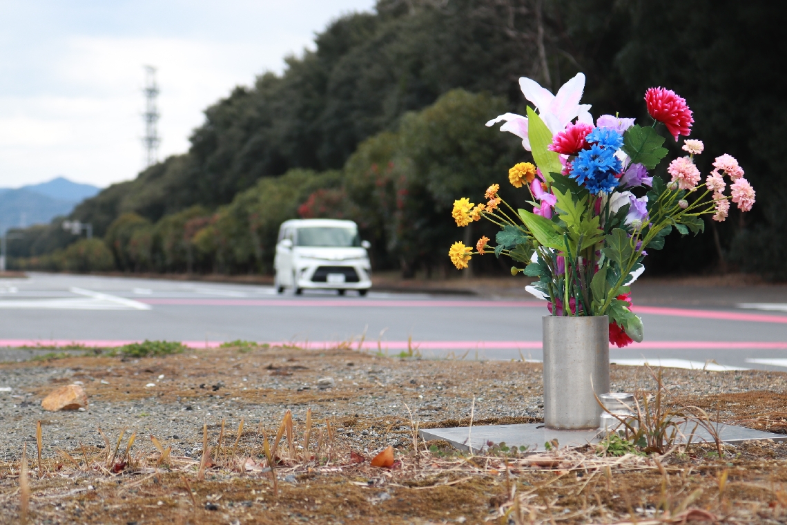 時速１９４キロの車が起こした死亡事故の現場。４年がたつ今も花が手向けられている＝７日、大分市大在