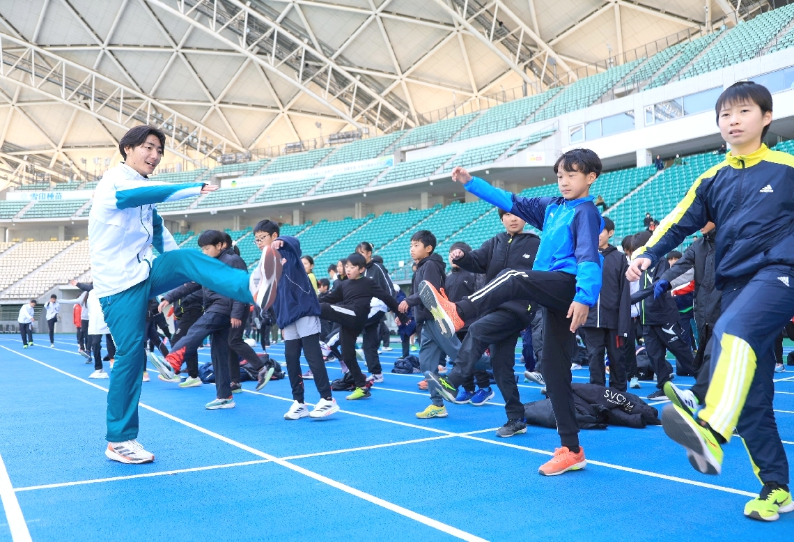 参加した子どもたちにストレッチなどを教える青山学院大の選手（左）＝クラサスドーム大分