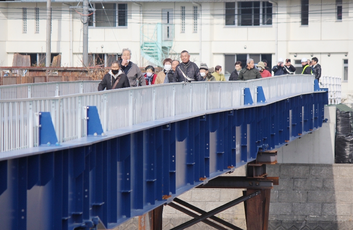 三郎丸橋上流に完成した仮設歩道橋の渡り初めをする住民ら