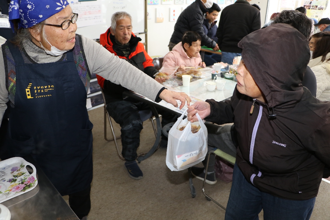 持ち帰りのうす焼きを地元住民に手渡す、佐賀関ふれあいカフェの住民スタッフ