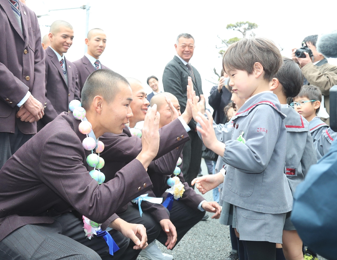 幼稚園児（右）から首飾りをかけてもらい、ハイタッチを交わす柳ケ浦ナイン
