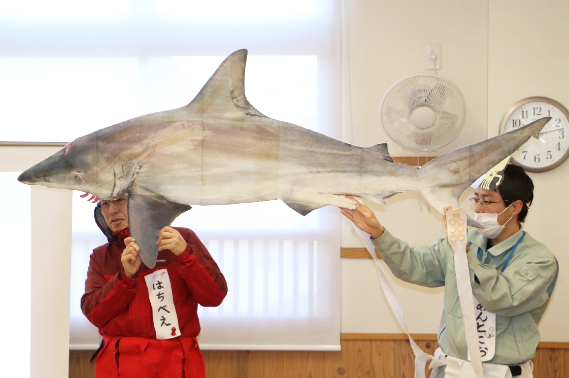 サメ教室でカマストガリザメの実物大パネルを見せながら説明する県と大分市の職員