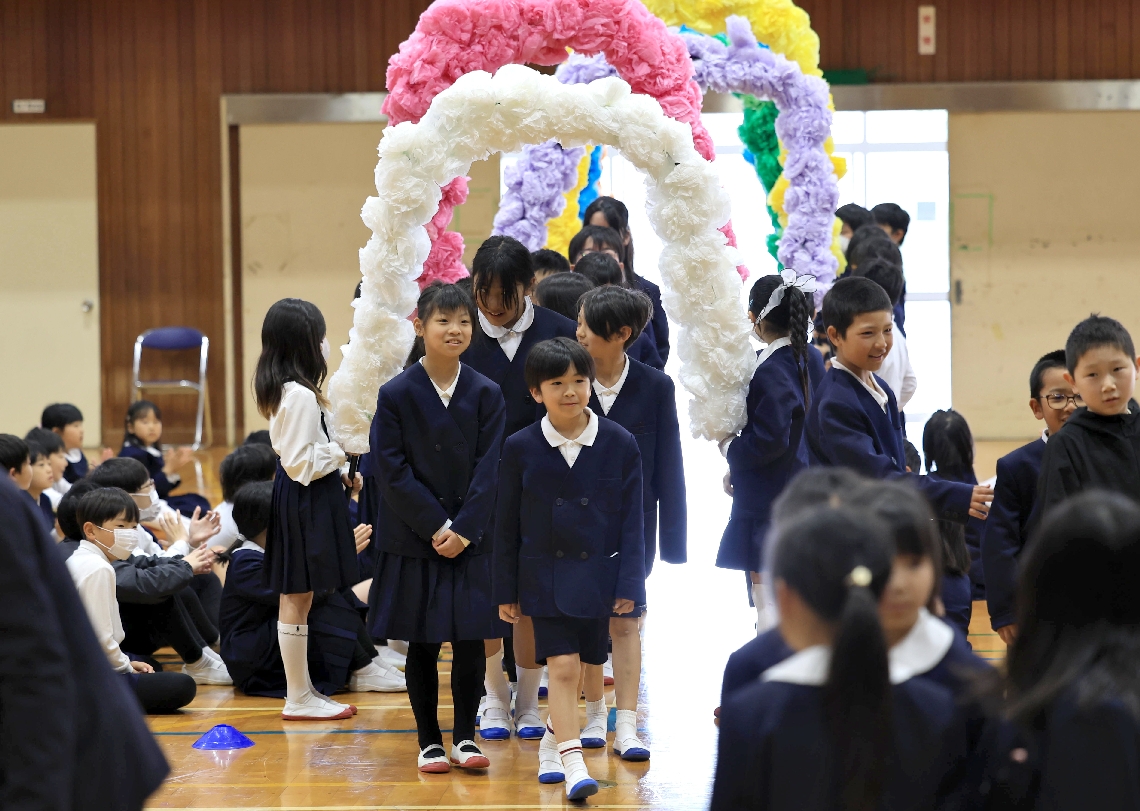 アーチをくぐって出迎えを受ける旭日、小原両小出身の児童たち＝８日、国東市の国東小