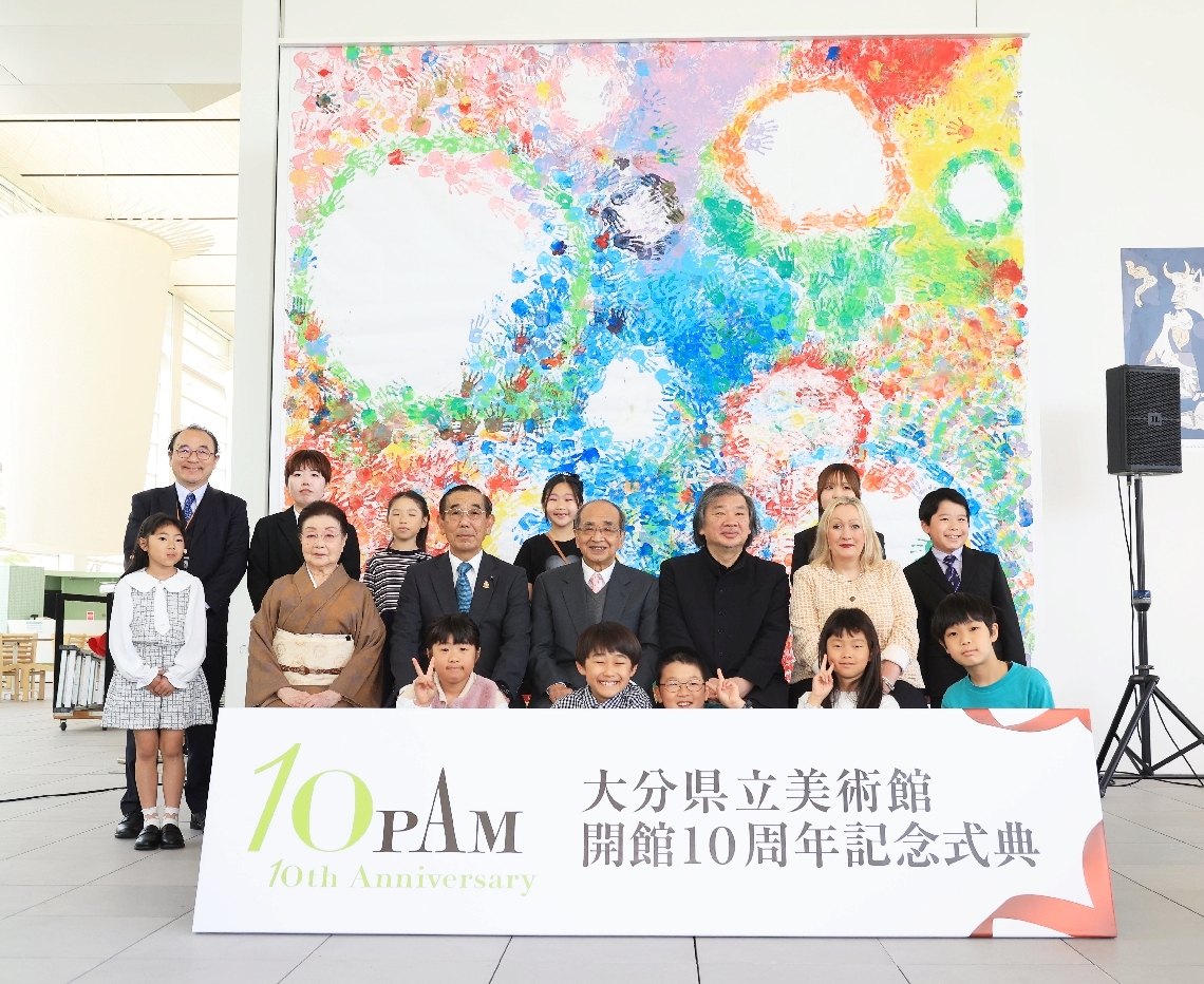 開館１０周年の記念モニュメントの前で、記念撮影に臨む式典関係者ら＝２６日、大分市寿町の県立美術館