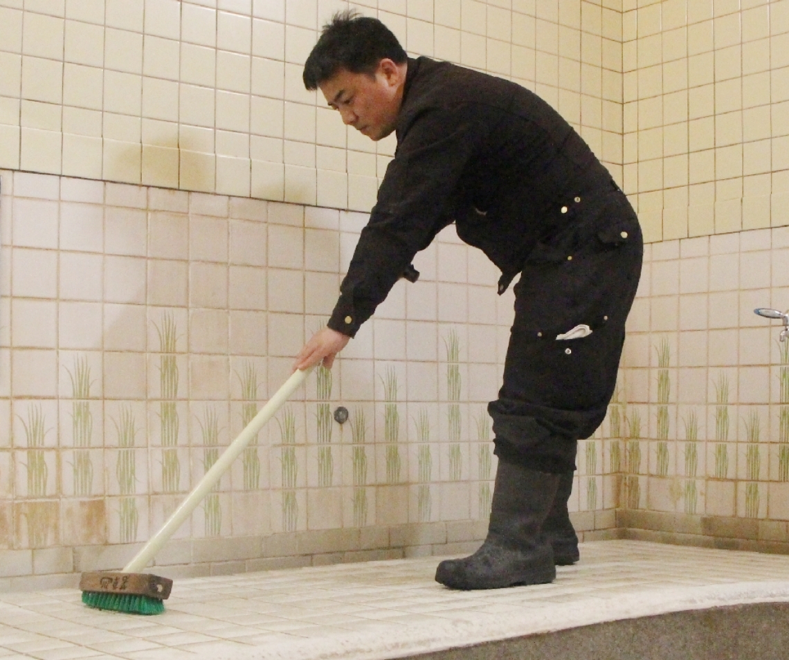 デッキブラシを使い、共同温泉のタイルを磨く清掃業者＝４月、別府市若草町の若草温泉