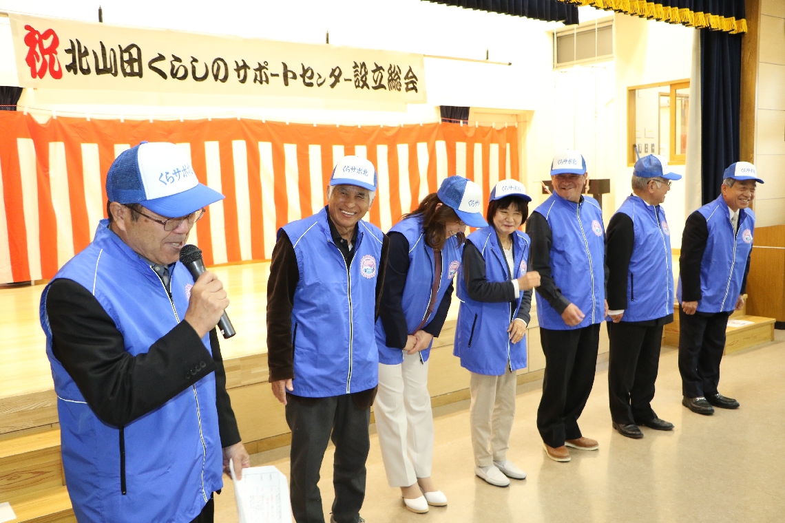 設立総会で、そろいの服装で自己紹介する北山田くらしのサポートセンターの役員＝玖珠町戸畑の北山田自治会館