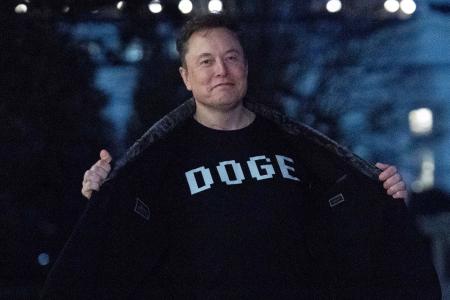 政府効率化省を意味する「ＤＯＧＥ」の文字が書かれたＴシャツを見せるマスク氏＝３月、ワシントン（ＡＰ＝共同）