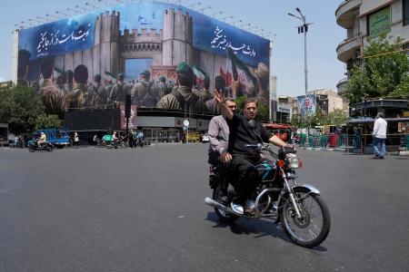 １４日、イランの首都テヘランで、反イスラエルの巨大看板を背にＶサインをする男性（ＡＰ＝共同）