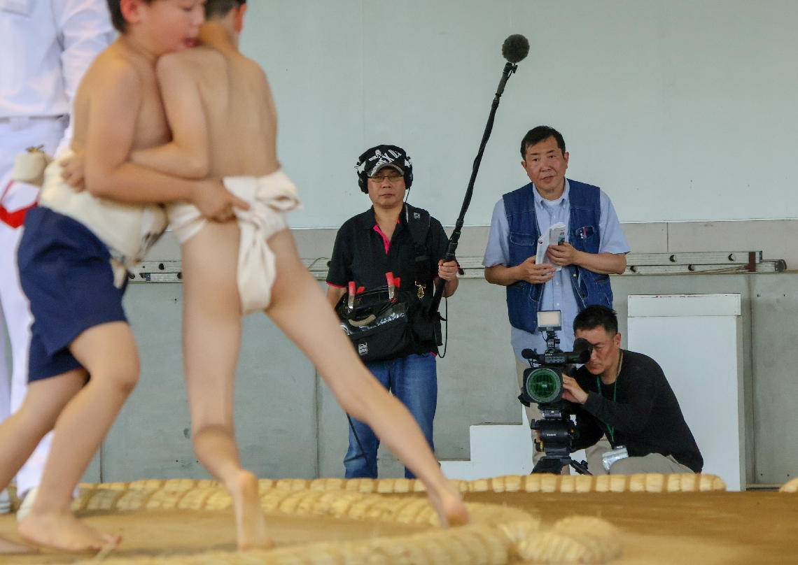 「わんぱく相撲双葉山杯」で熱戦を繰り広げる子どもたちを撮影する松村克弥監督（右から２人目）ら＝宇佐市川部の市総合運動場相撲場