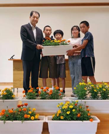 群馬県上野村の村立上野小で開かれたマリーゴールドの引き渡し式で、写真に納まる黒沢八郎村長（左端）と児童たち＝１８日午前