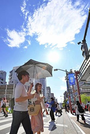 真夏のような日差しの中、日傘を差して歩く人たち＝６月、東京・浅草