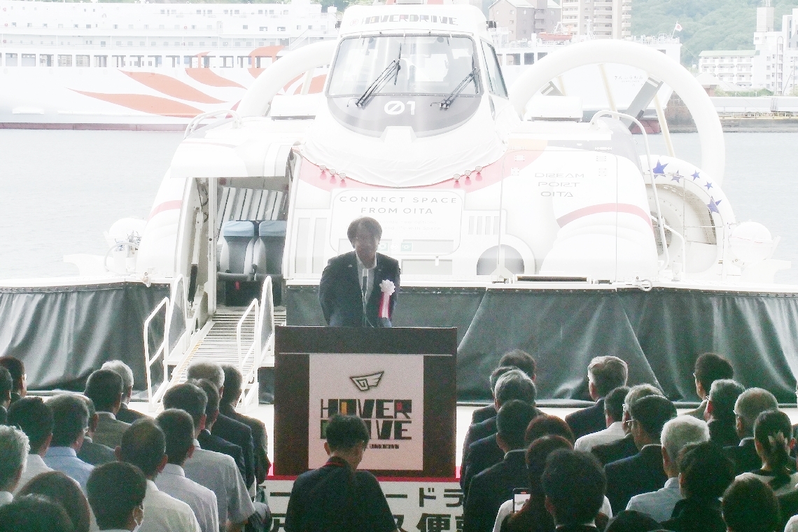 式典には約１４０人が出席。ホーバークラフトの前であいさつする小田典史社長＝１９日午前、大分市駄原