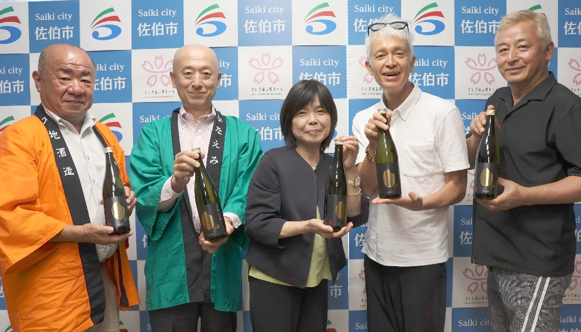 完成した「ふっかきまい」を手にPRする（左から）大地酒蔵の池田司専務、池田敬社長、冨高国子市長、マーク・パンサーさんら＝佐伯市役所