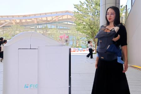赤ちゃんを抱いた女性にロボット（左）が近づいてサービスを提供する実演＝２４日午後、東京都港区