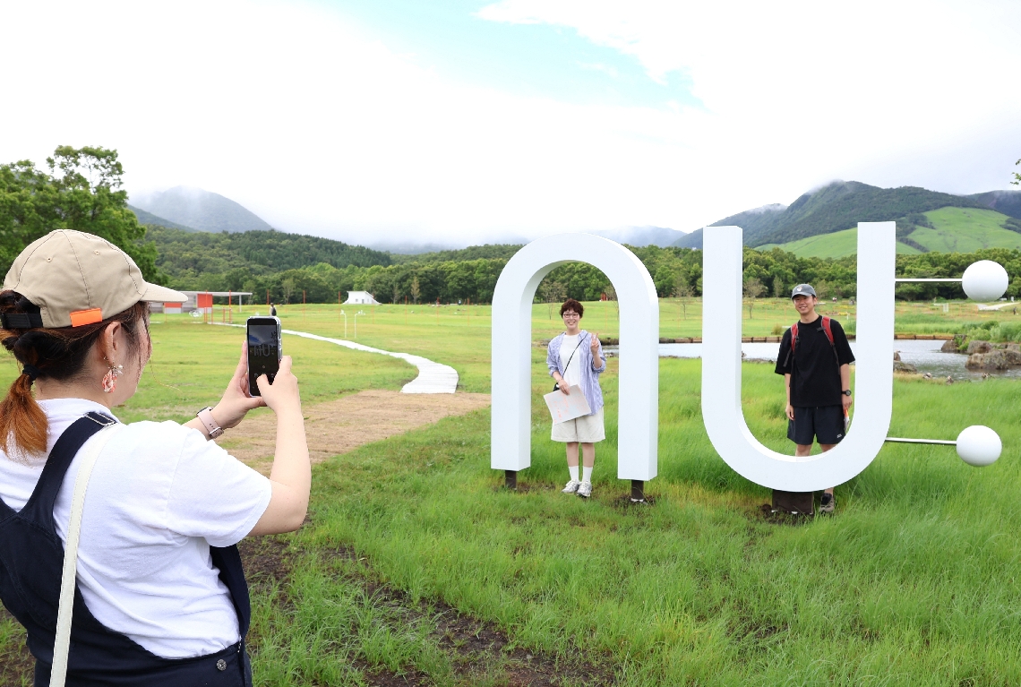 草原を見渡すモニュメントの前で記念写真に納まる来場客＝九重町田野の「ＮＵ：ＫＵＪＵ」