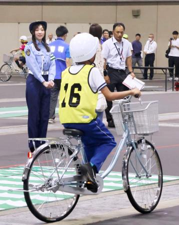自転車の乗り方などを競う大会で、実技テスト中の参加者（手前）を見守る愛知県警交通安全大使の須田亜香里さん（奥左）＝２９日午前、名古屋市
