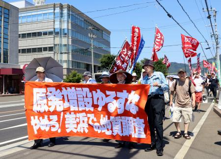 関西電力原子力事業本部（左奥）周辺で行進する市民団体＝３０日午後、福井県美浜町