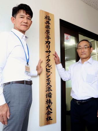 福井県原子力リサイクルビジネス準備株式会社の事務所入り口に看板を設置する来馬克美社長（右）ら＝１日午前、福井県敦賀市