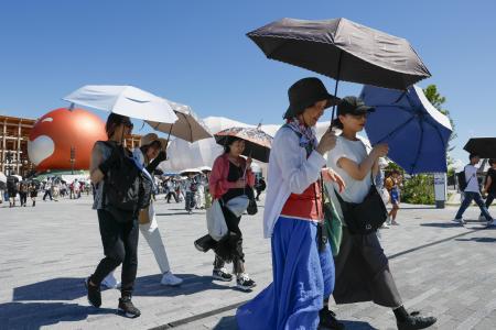 厳しい暑さの大阪・関西万博の会場で、日傘を差して歩く人たち＝７月、大阪市此花区の夢洲