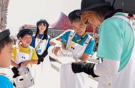 屋外で働くスタッフらにスポーツドリンクをついで回る仕事体験の小学生ら＝３日午後、大阪市此花区の夢洲