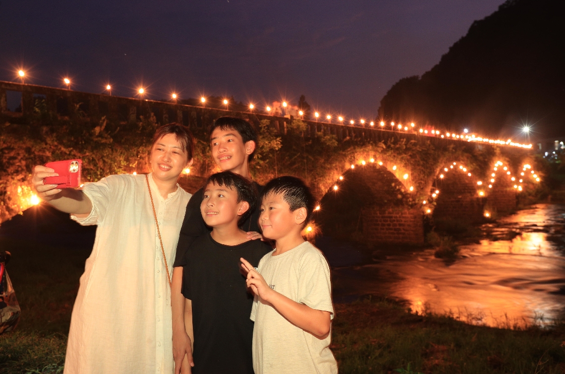 たいまつの炎で浮かび上がった原尻橋を背景に記念撮影をする人たち＝１４日夜、豊後大野市緒方町
