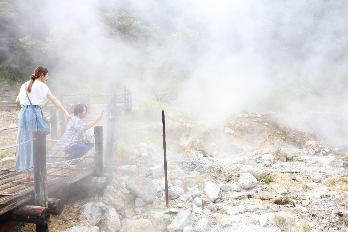 あちこちから湯気が上がる小松地獄の景色を楽しむ観光客