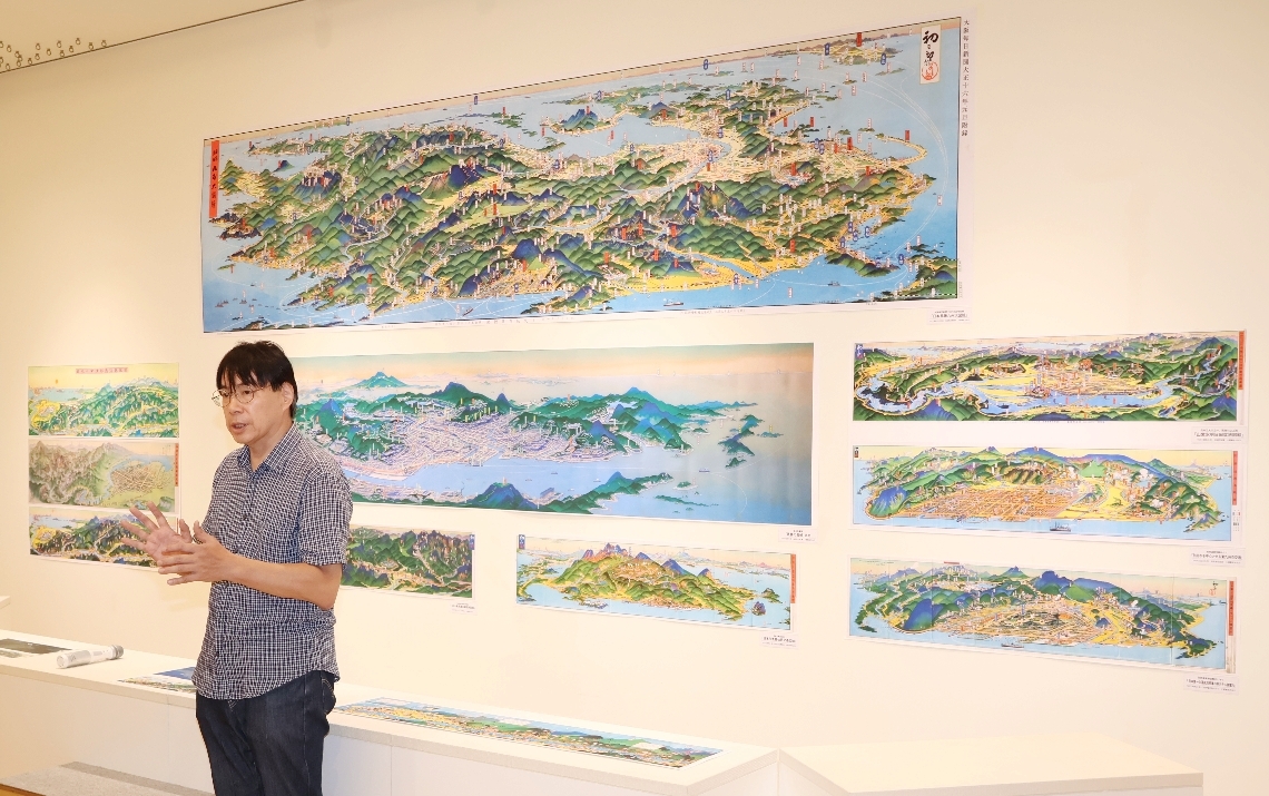 大胆なデフォルメを施した吉田初三郎の観光鳥瞰図（写真は多くの吉田の作品を出展した益田啓一郎さん）＝玖珠町森の久留島武彦記念館