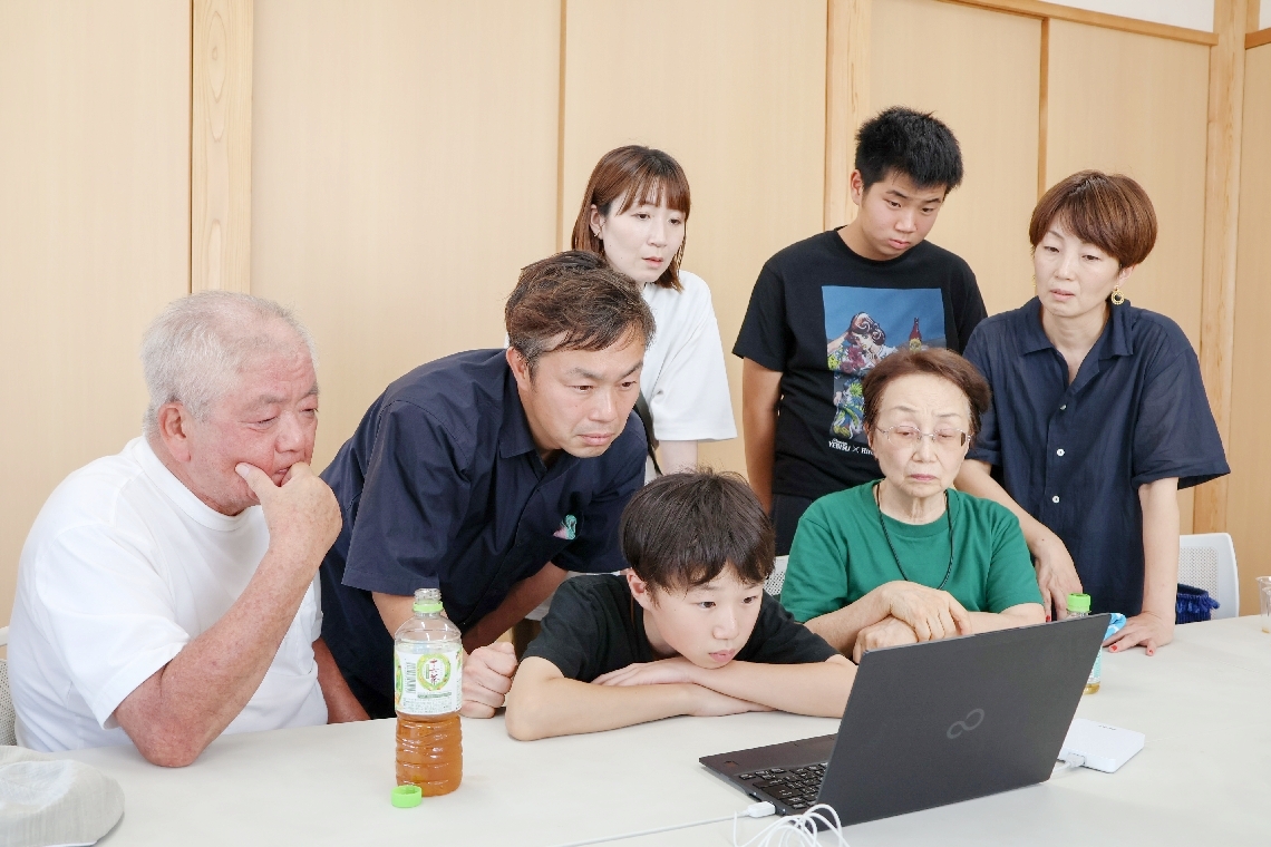 園部勇さんが写った映像に見入る長女の山本晶子さん（前列右端）ら家族＝宇佐市森山の教覚寺