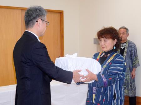 遺骨を受け取る釧路アイヌ協会の桃井芳子会長（右）＝３０日午前、北海道釧路市