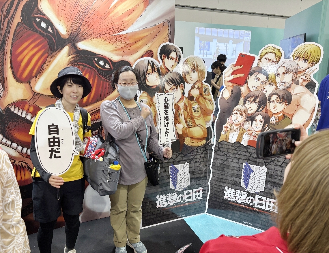 大阪・関西万博で訪日客らに大分県の魅力をＰＲするイベントが３日、始まった。日田市大山町出身の諫山創さんの人気漫画「進撃の巨人」のパネルを前に記念撮影する人たち＝大阪市内