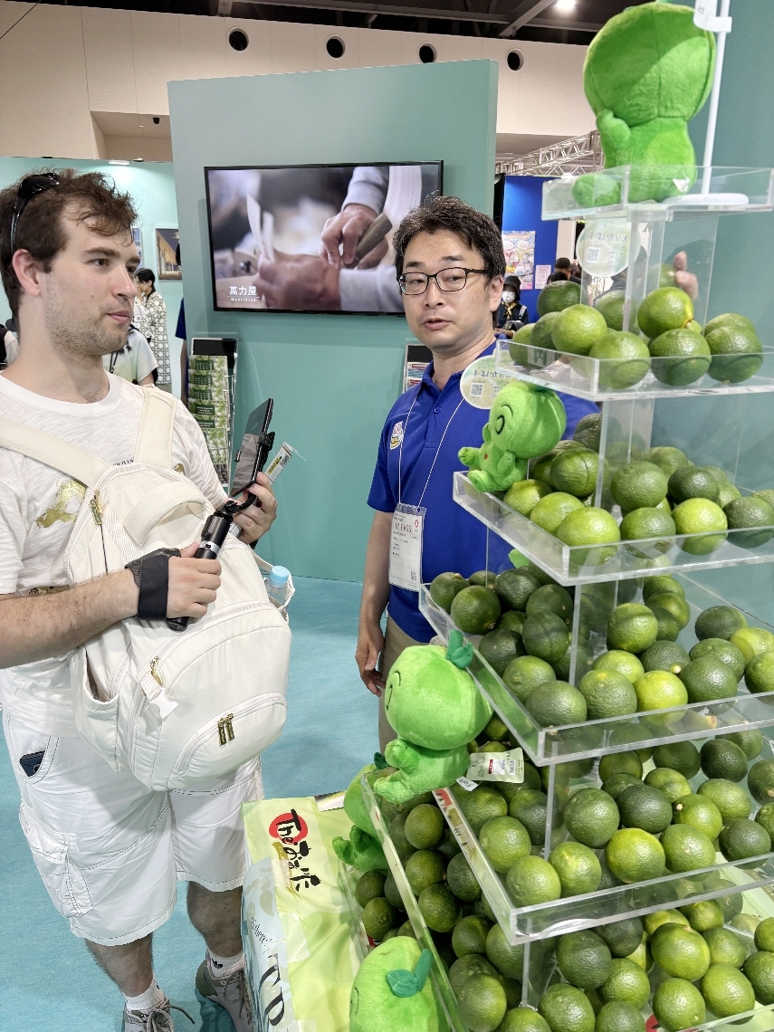 訪れたアメリカ人（左）に県特産カボスの特長を伝える県職員