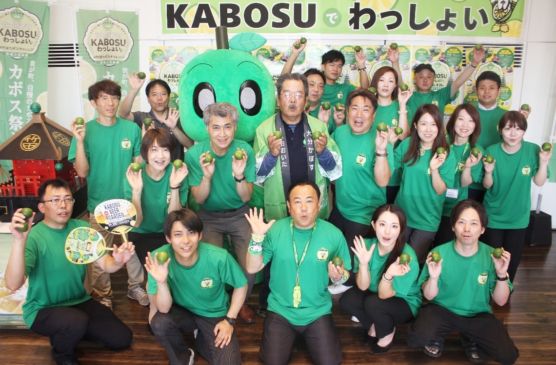 オープニングイベントで、「カボスでわっしょい！」とのかけ声を上げて記念写真に納まる関係者＝竹田市竹田町の市城下町交流プラザ