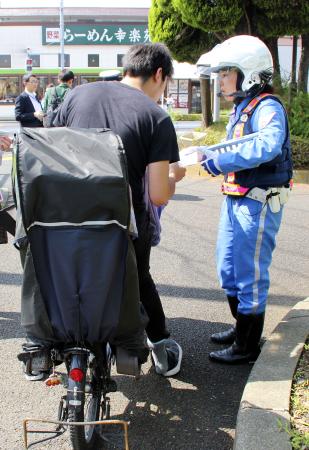 自転車利用者に注意喚起のチラシを配る警視庁の警察官＝６月、東京都葛飾区