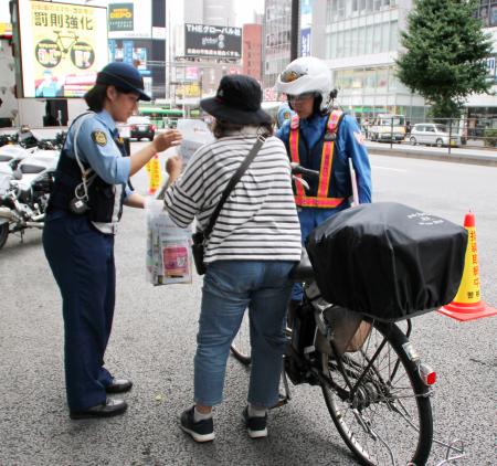 自転車利用者に啓発用のチラシを配る警察官＝４日午前、東京都新宿区