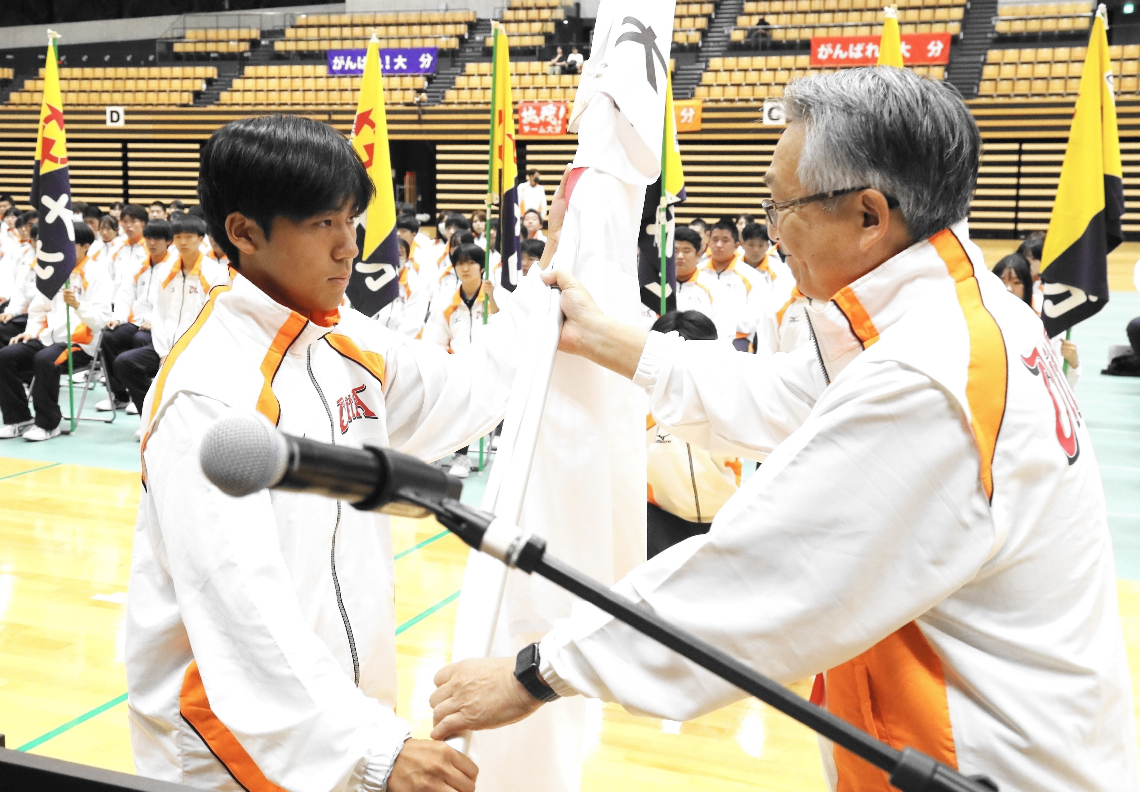 麻生会長から団旗を受け取るテニス少年男子の安藤（左）＝クラサス武道スポーツセンター