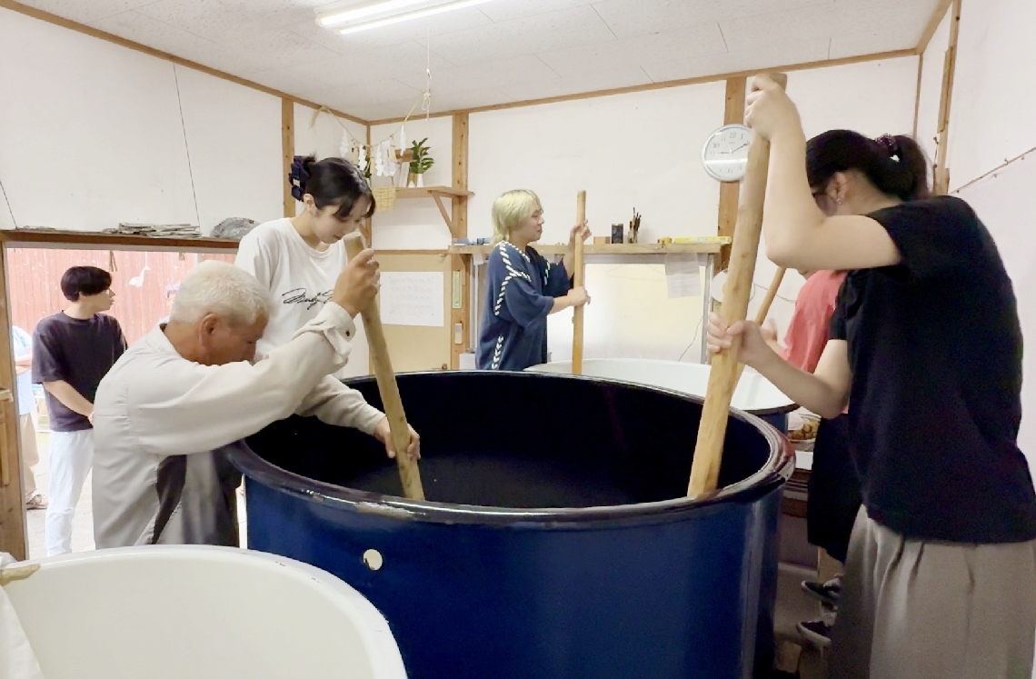 容器に入れた米などをかき混ぜる「櫂入れ」をする参加者