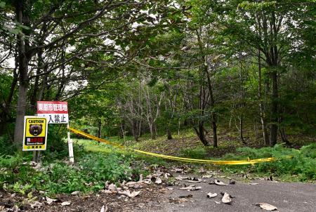 林道の入り口に張られた規制線とクマ出没に注意を呼びかける看板（左端）＝５日午前、宮城県栗原市