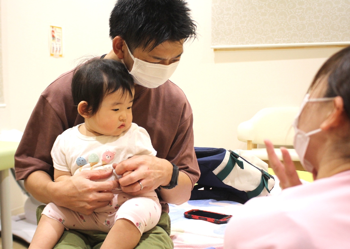 看護師から接種について説明を受ける平田浩太さんと彩峰ちゃん＝竹田市玉来の市立こども診療所