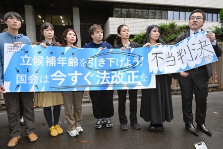 東京地裁による被選挙権年齢引き下げ訴訟判決を受け「不当判決」などと書かれた紙を掲げる原告団＝２４日午後、東京・霞が関