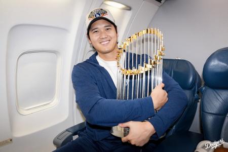 ロサンゼルスへ移動する機内で優勝トロフィーを抱くドジャース・大谷（ドジャースの球団公式Ｘから）