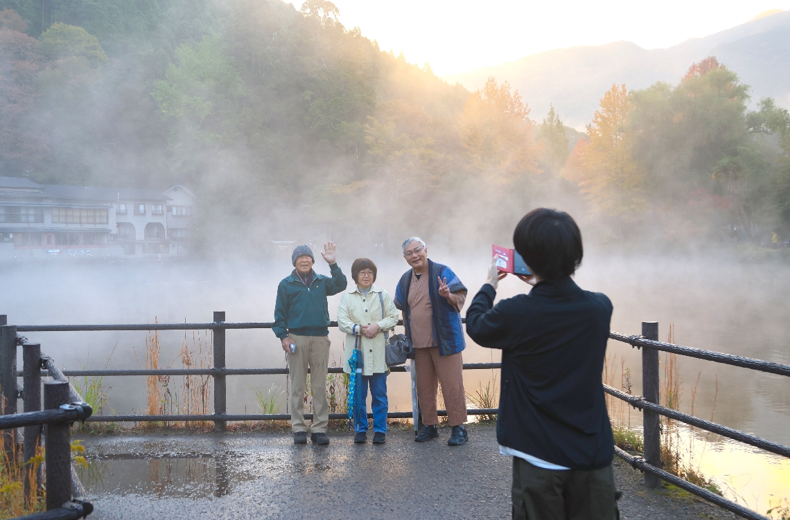湖を背に記念撮影をする人たち＝６日午前６時５５分、由布市湯布院町