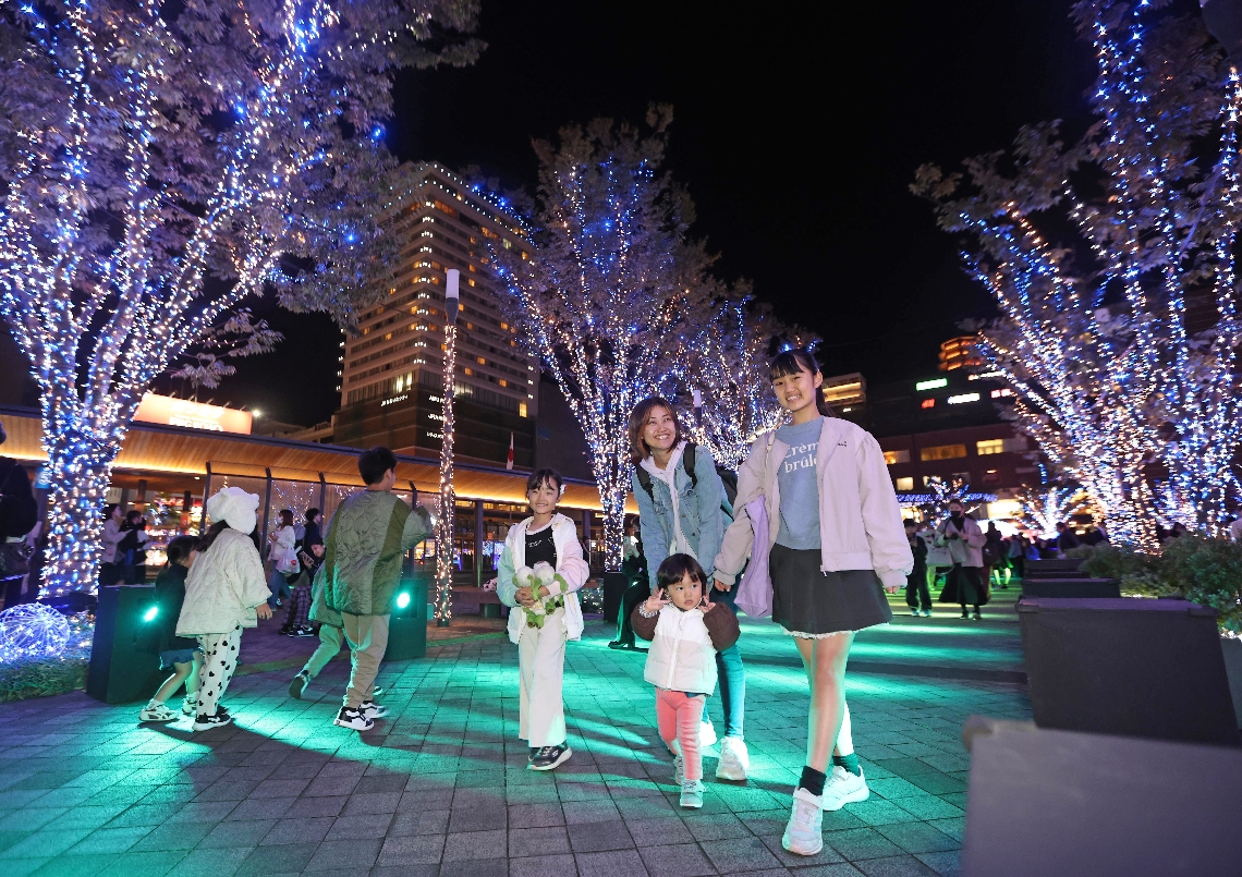ＪＲ大分駅府内中央口広場に点灯したイルミネーションを楽しむ家族＝７日夜、大分市末広町