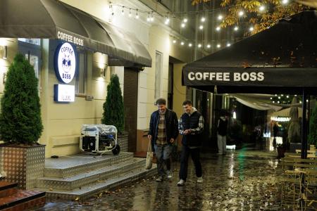 ウクライナ北部チェルニヒウで、停電中に発電機を使って営業するカフェの前を歩く若者＝１０月（ロイター＝共同）