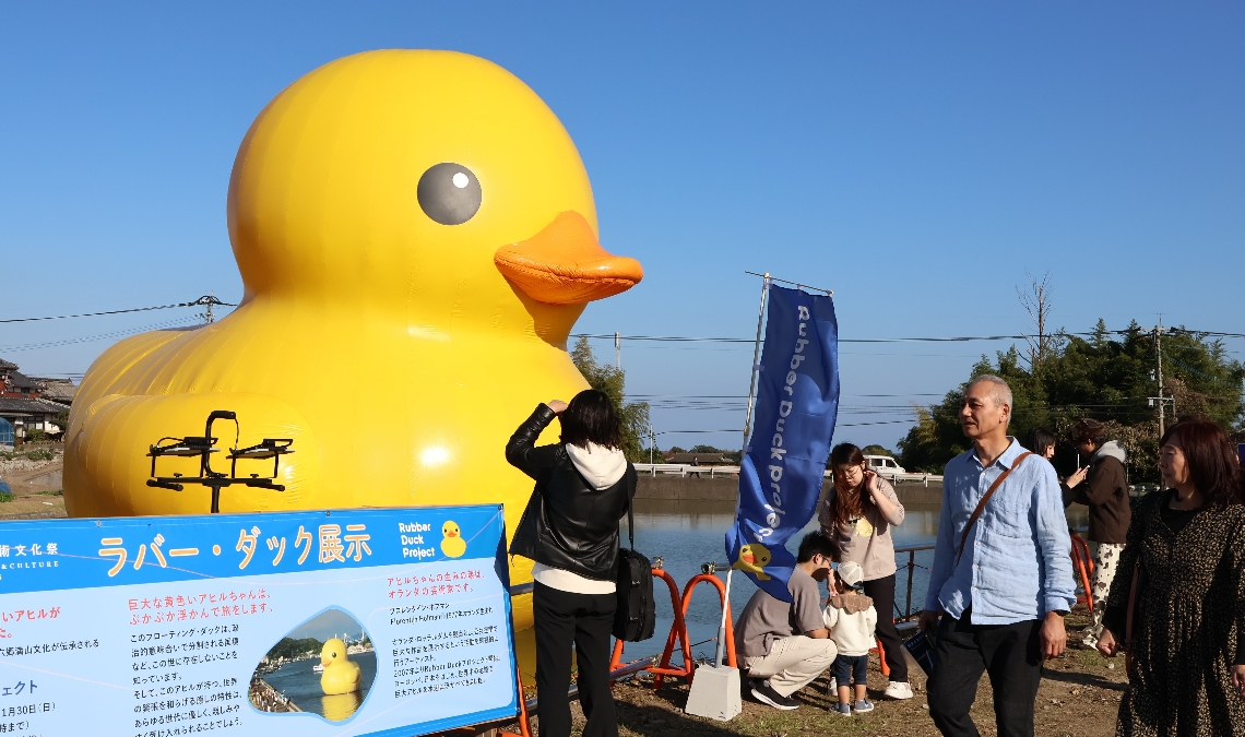 ラバー・ダックの前で記念撮影を楽しむ来場者＝国東市国東町の迫池