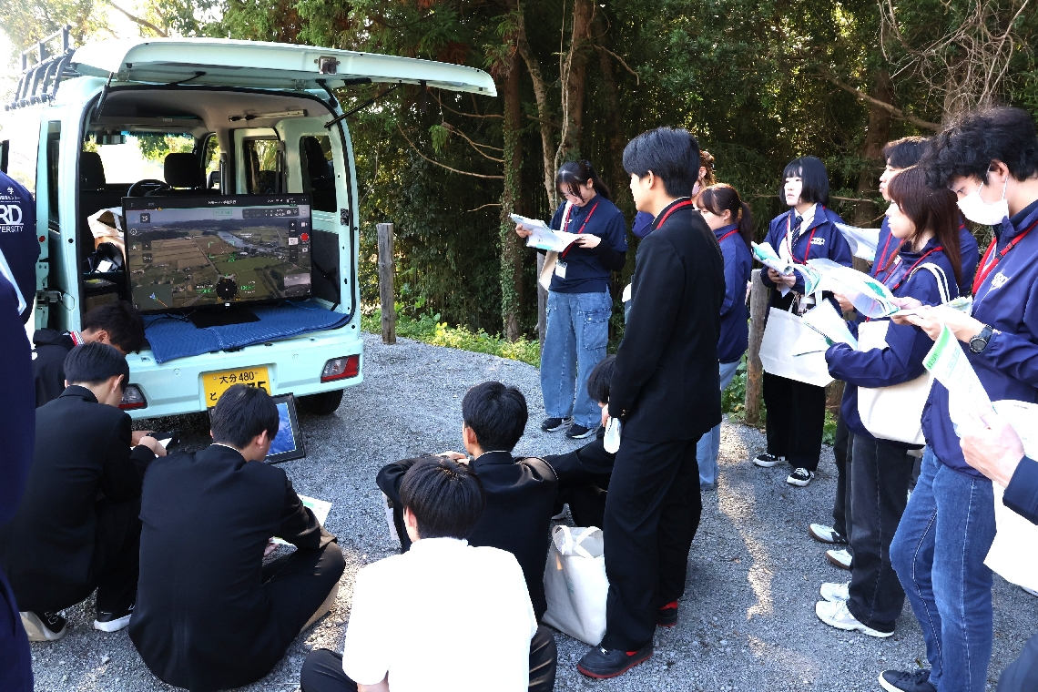 ドローンの空中映像を見ながら河川改修の様子を見る大学生と生徒