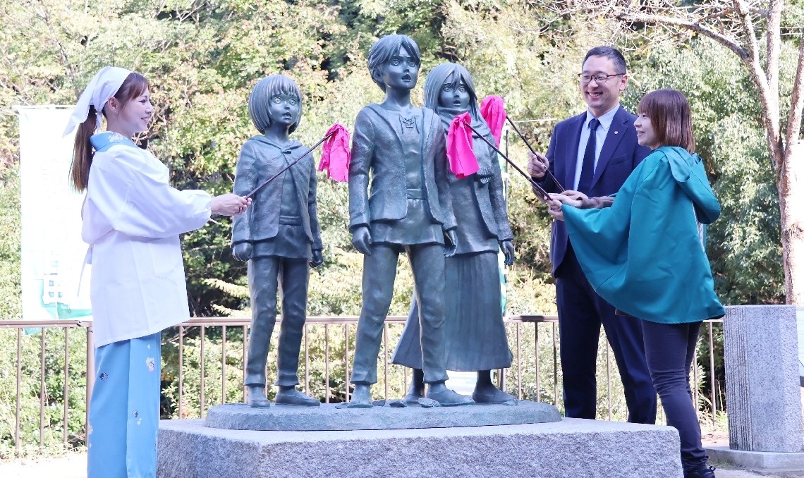 「進撃の巨人」主人公らの銅像のほこりをはたきで取り除くファン＝日田市大山町の大山ダム